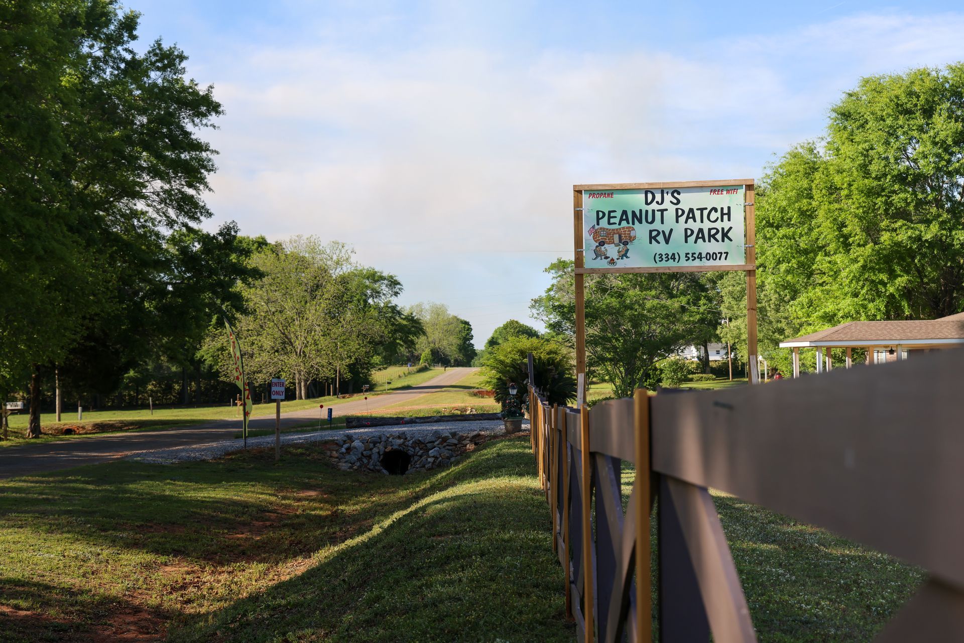 Community park path with a sign beside a fenced walkway and trees in the background