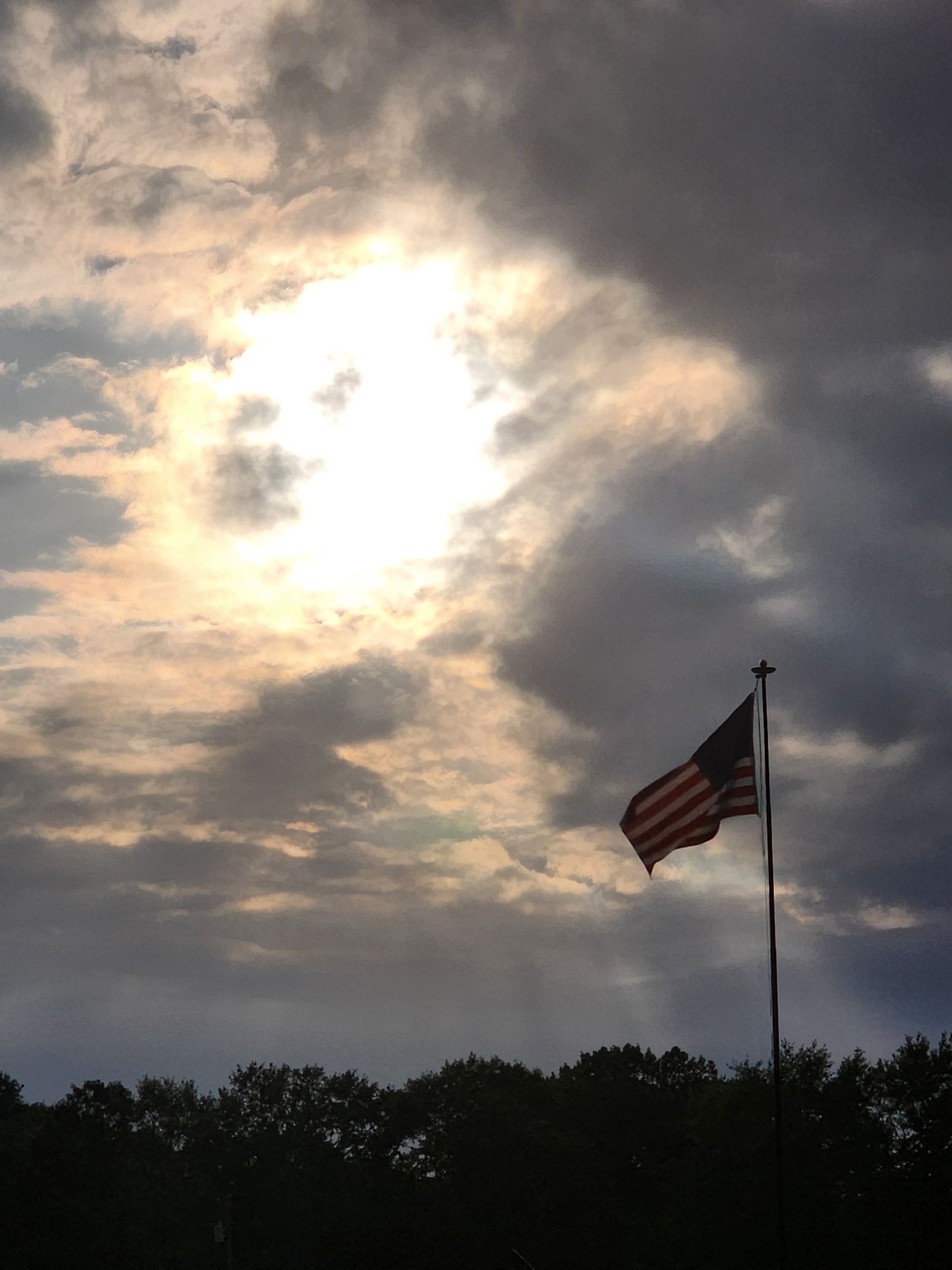 American flag on a pole silhouetted against a cloudy, glowing sunset sky