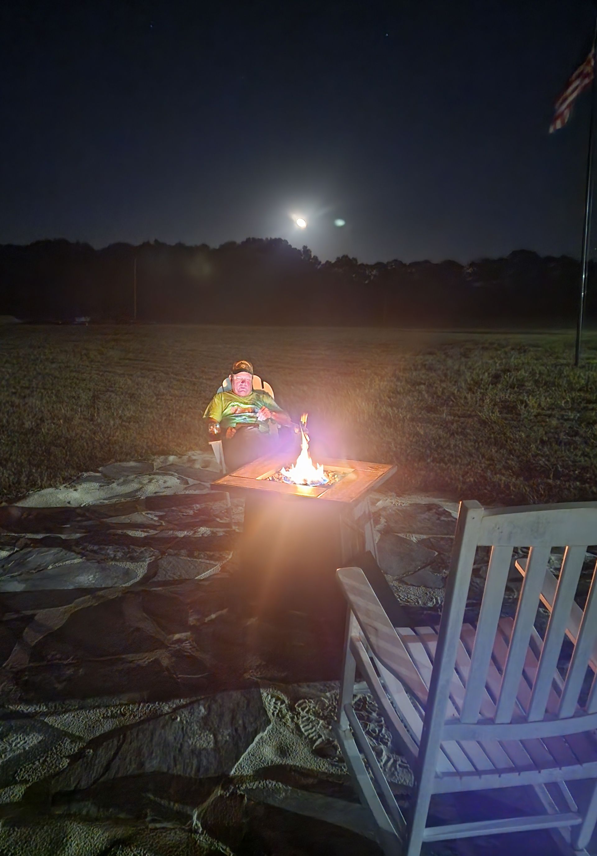 Person sitting by a small campfire in a dark field at night, with moonlight overhead.