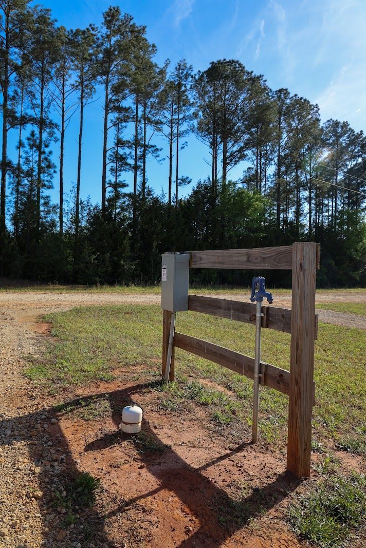 Wooden sign frame beside a dirt path in a grassy field with pine trees under a blue sky.