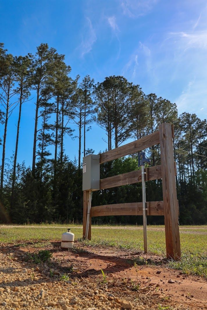 Wooden sign in a grassy field with tall pine trees under a bright blue sky
