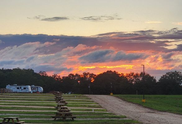 Sunset over a campground with RVs, picnic tables, and a gravel road under colorful clouds