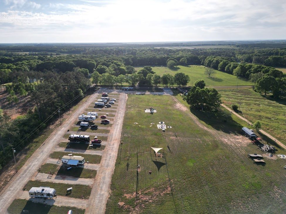Aerial view of a parking area beside a grassy field and trees under a bright sky