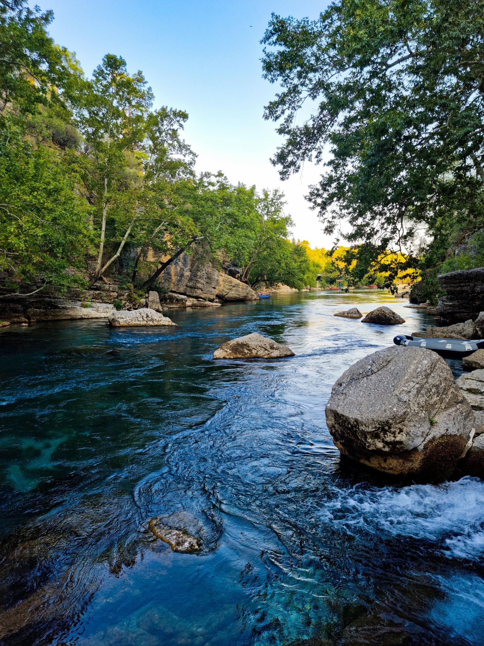 Clear blue river flowing through a rocky forested gorge with sunlight in the distance