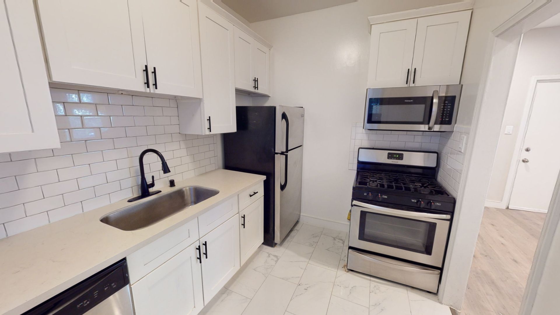 Modern kitchen with white cabinets, stainless steel appliances, and white tiled backsplash.