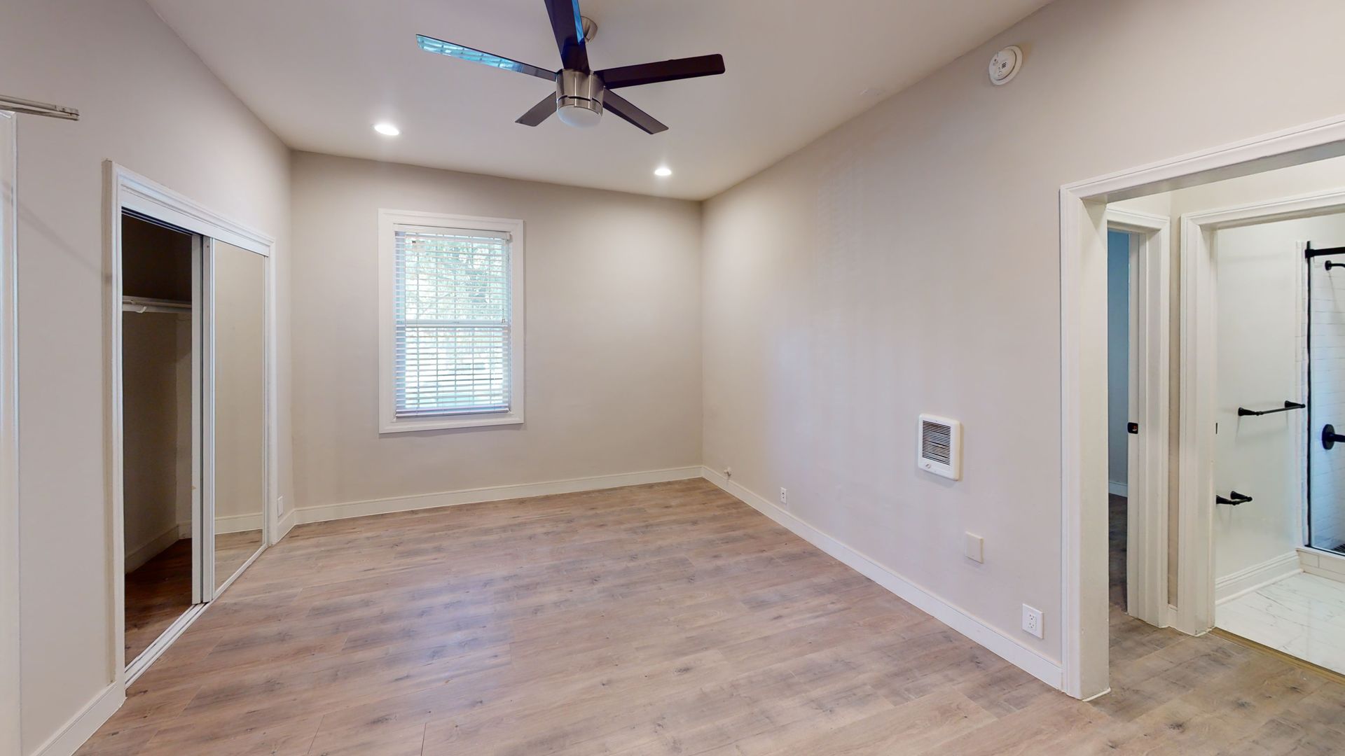 Empty bedroom with light wood flooring, closet, small window, and doorway to bathroom.