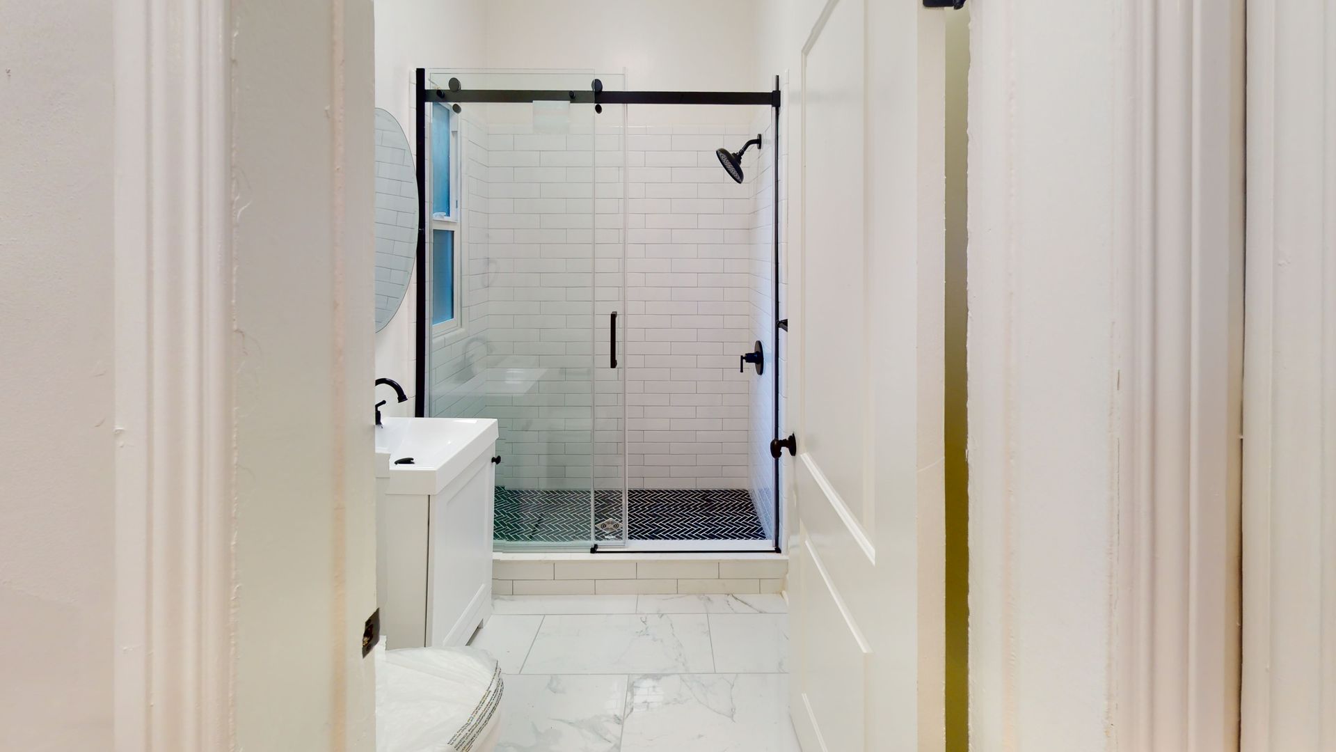 Bathroom interior with white walls, shower with glass door and black frame, white vanity, and marble floor.
