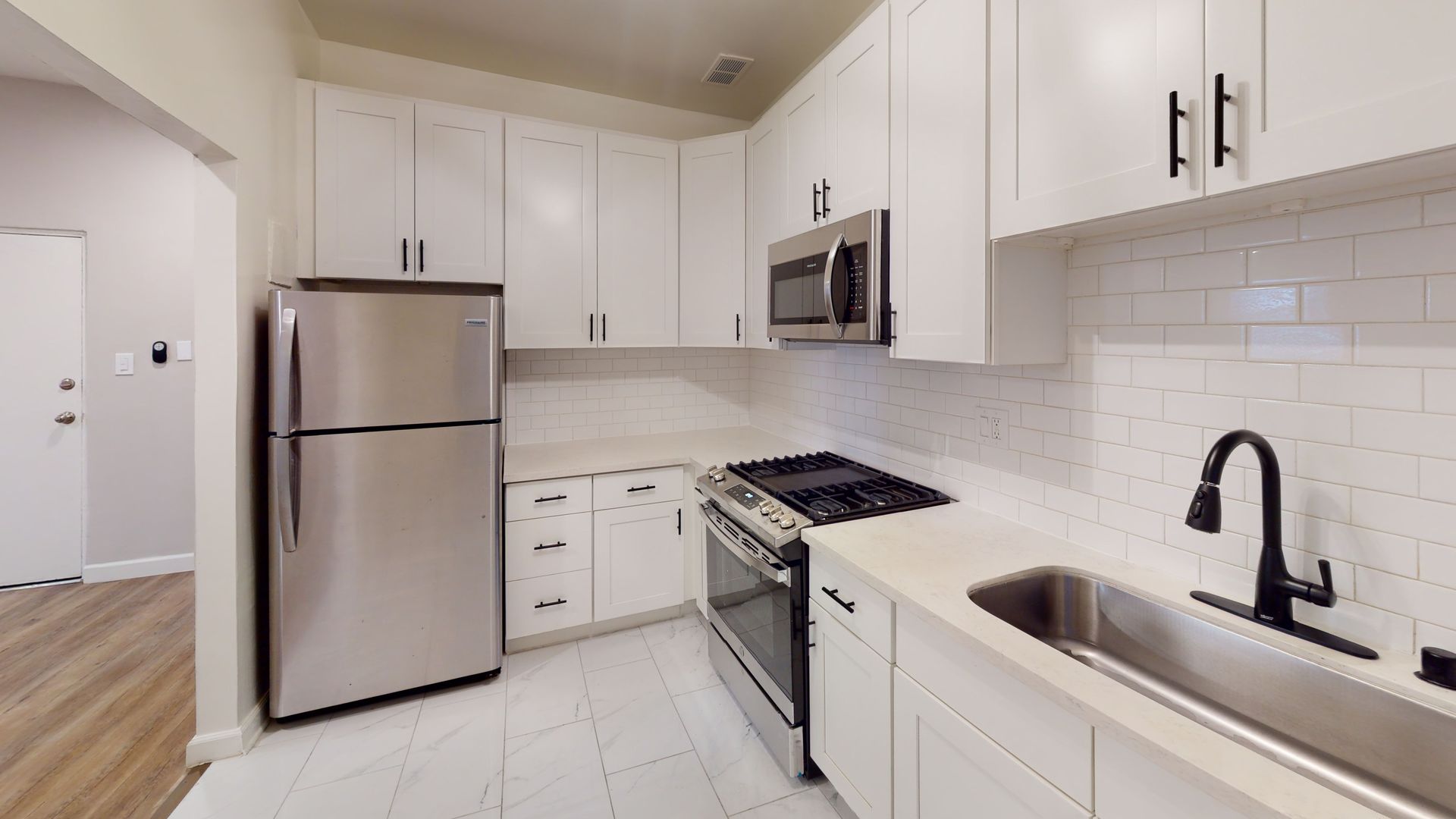White kitchen with stainless steel appliances, white cabinets, and subway tile backsplash.