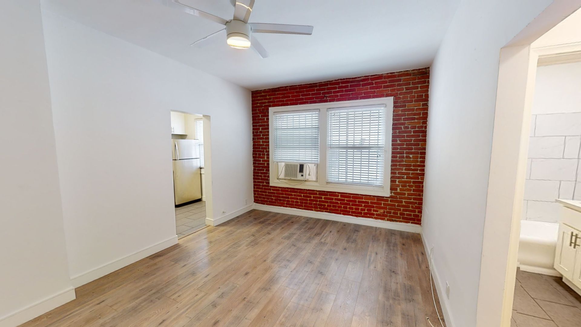 Empty room with brick accent wall, window, and wood-look flooring. White walls and door frames.