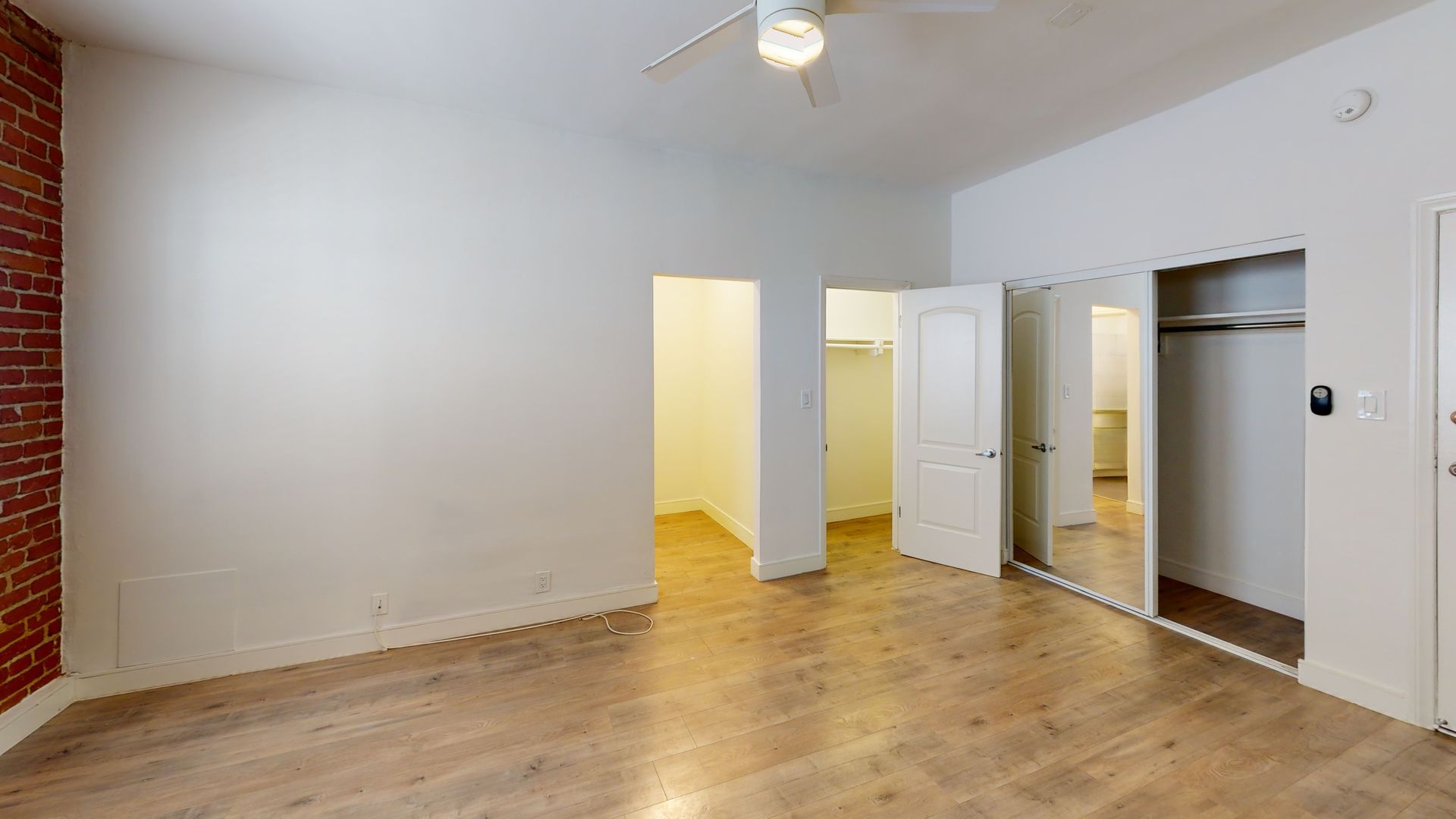 Empty room with wood floor, white walls, exposed brick, and closets.