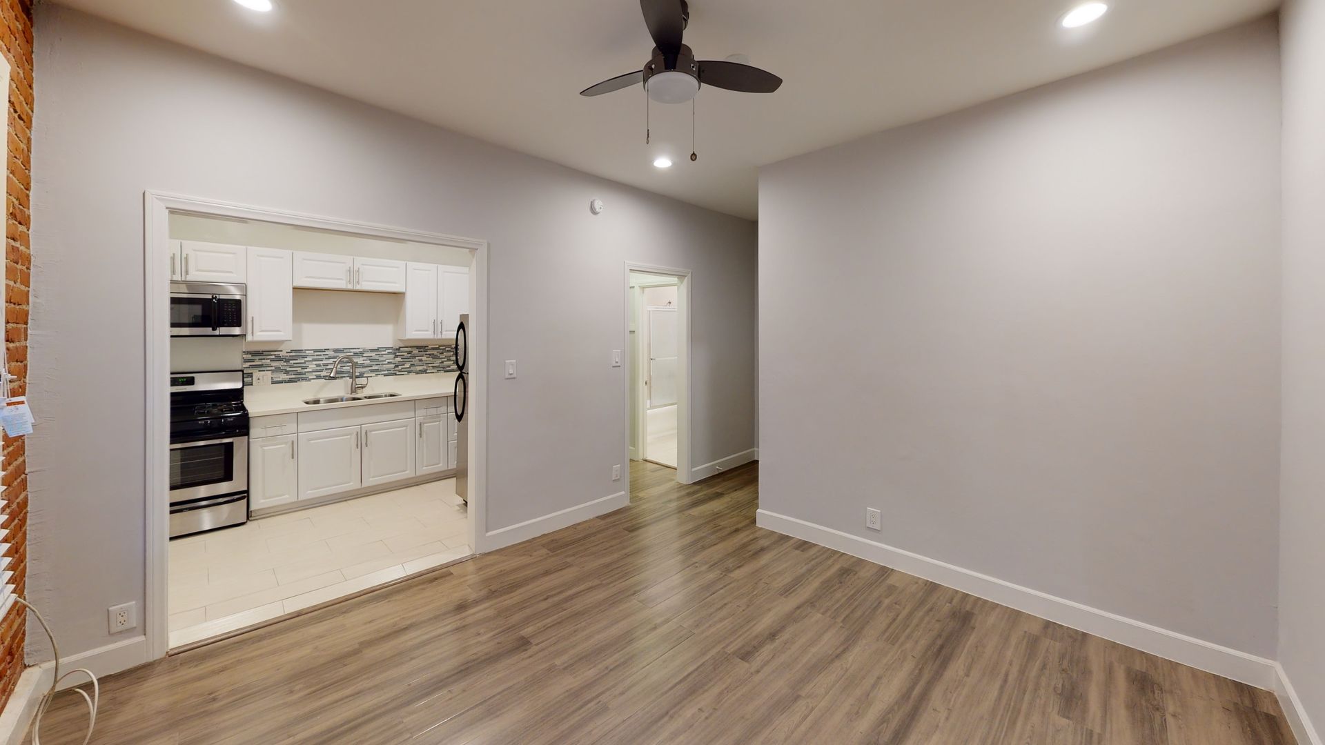 Living room with an open kitchen and hallway; hardwood floors, gray walls, ceiling fan.