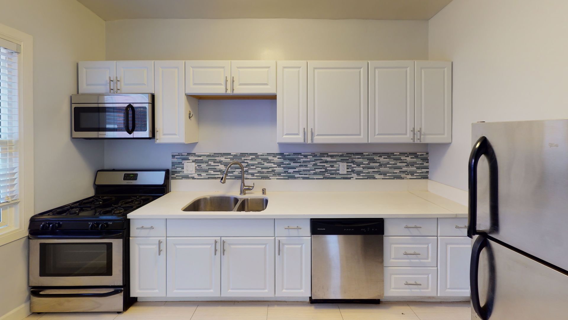 White kitchen cabinets, stainless steel appliances, and a mosaic backsplash.
