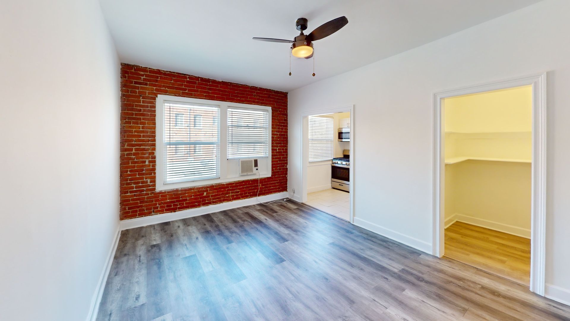 Empty room with exposed brick wall, window, gray wood floor, and open doorway.