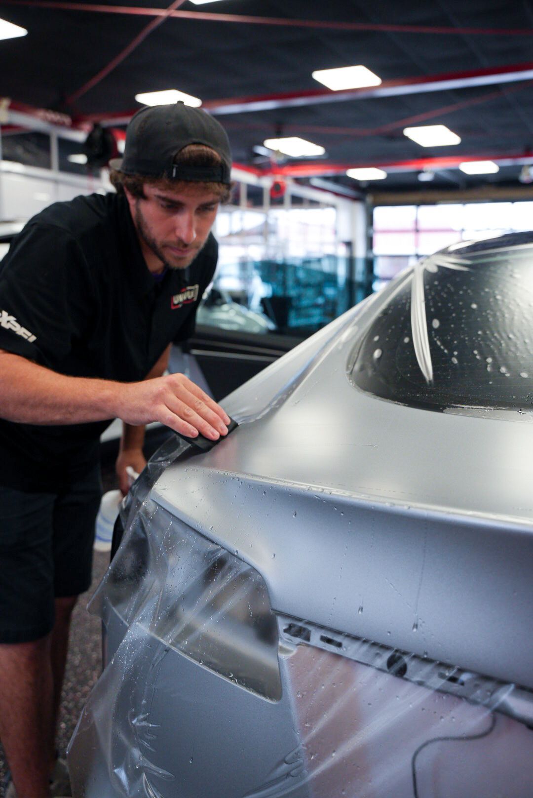 Man applying film to a car's surface in a garage, using his hand to smooth it.