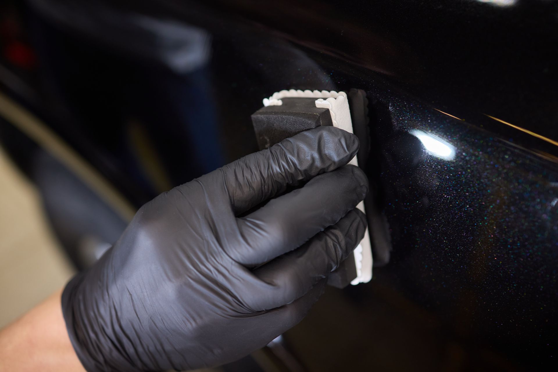 A person wearing black gloves is polishing a car with a sponge.