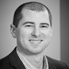 A man in a suit is smiling in a black and white photo.