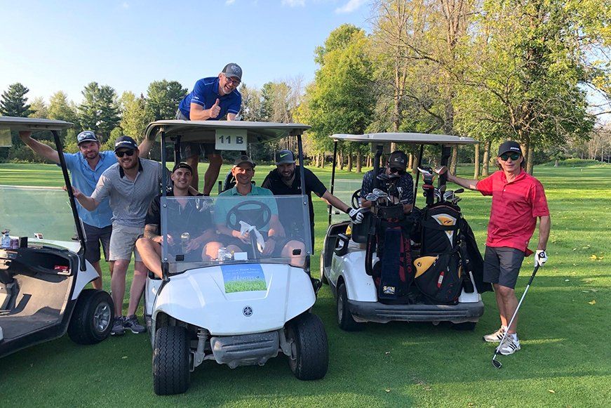 A group of men are standing next to golf carts on a golf course.