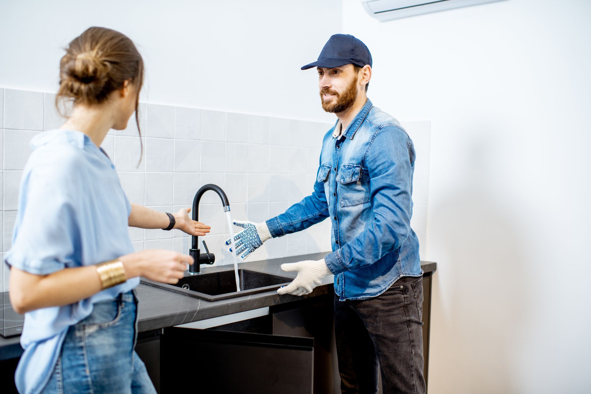 A man is showing a water flows in a kitchen sink while a woman looks on.