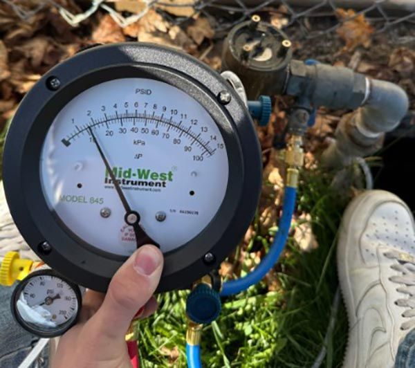 Hand holding a pressure gauge connected to irrigation pipes; gauge reads 45 kPa.