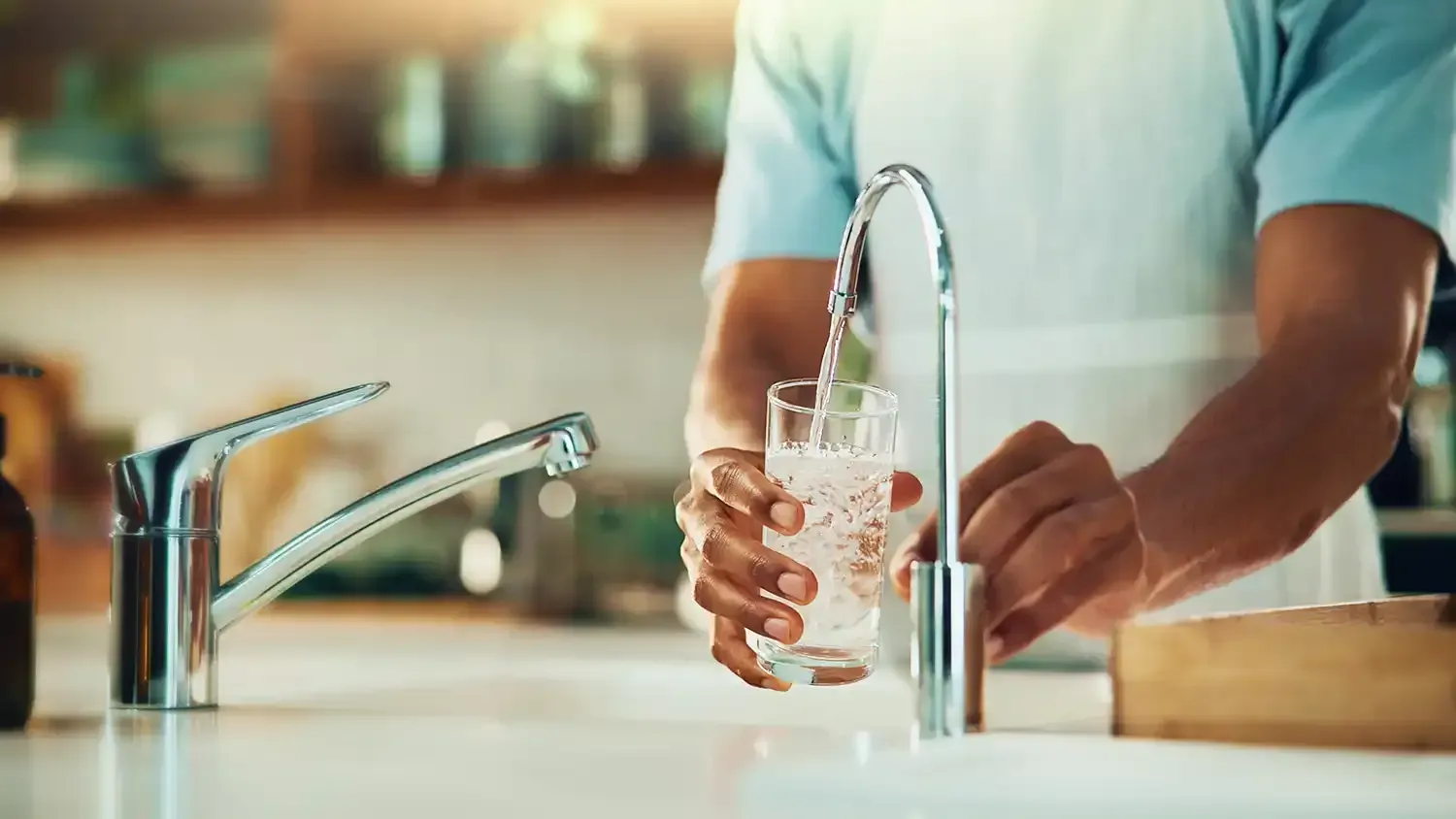 Person filling a glass with water from a kitchen faucet