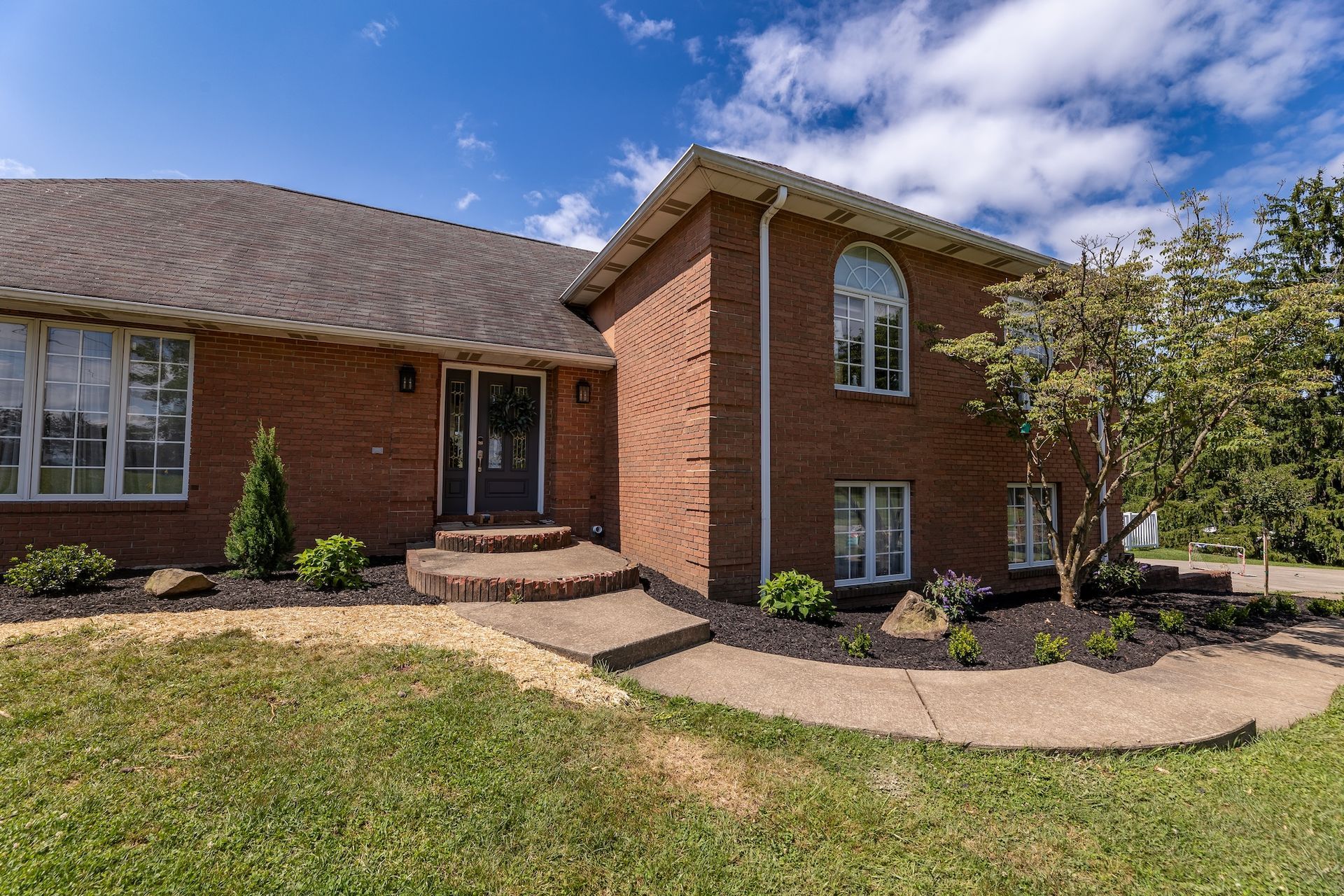Front yard of a suburban house with shrubs, mulch landscaping, and a garage driveway.