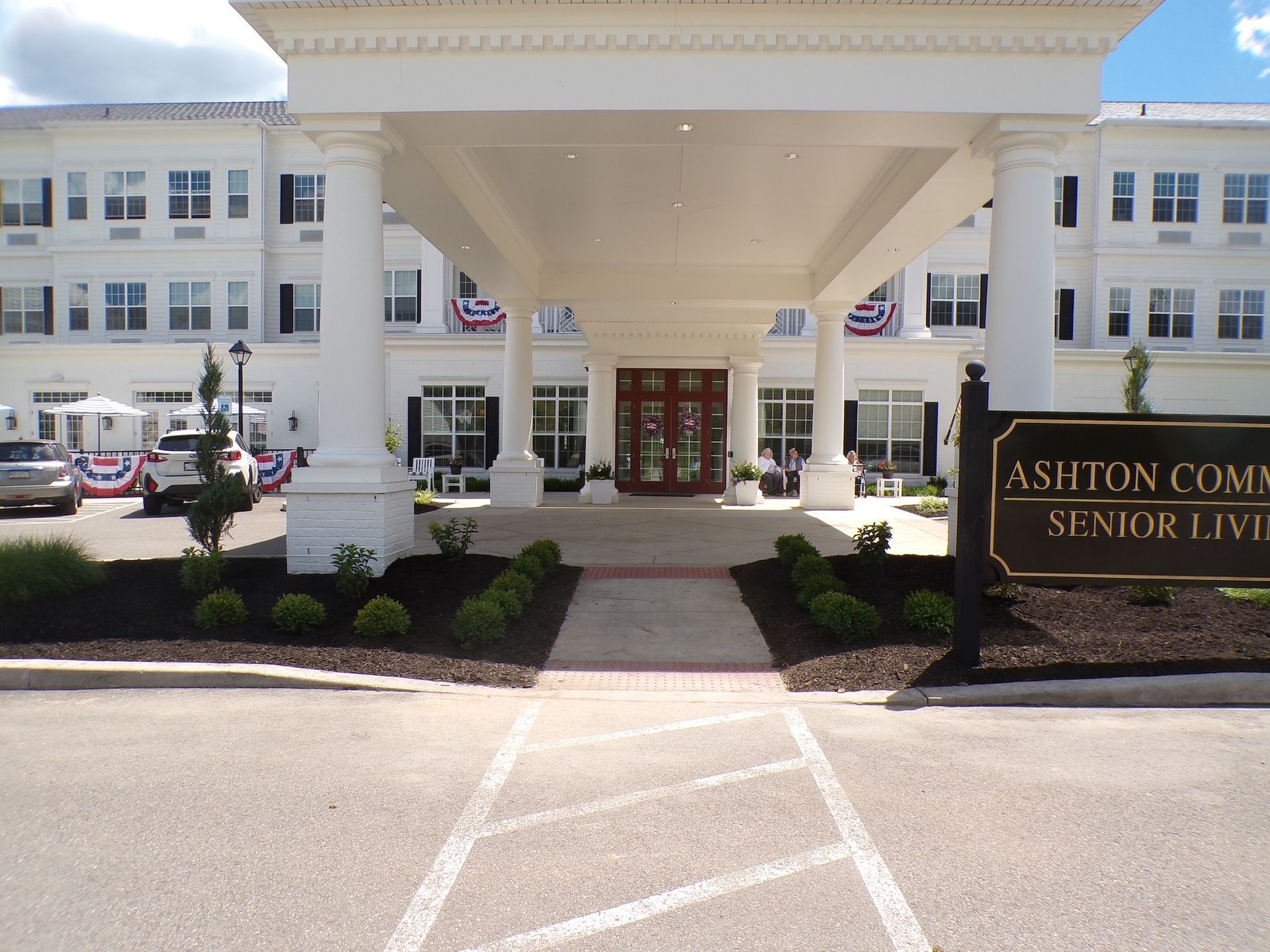 Entrance of Ashton Commons Senior Living with white columns and landscaped drive-up area