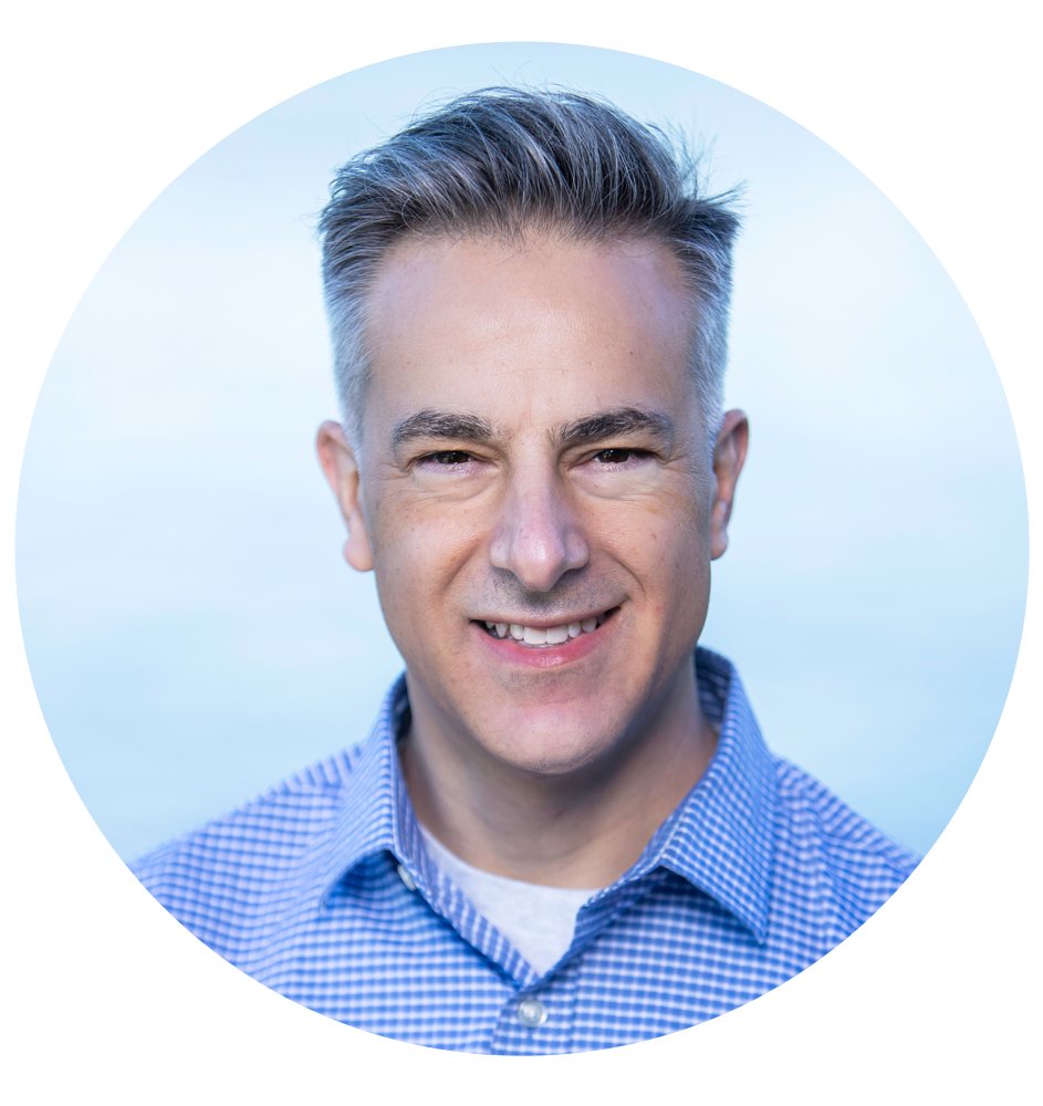 Paul DelGrosso Man in a blue button-down shirt smiles; gray hair, light blue background.