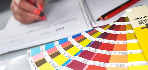 Rachael Haywood is sketching a logo Person writing on paper with colorful fan of paint swatches.