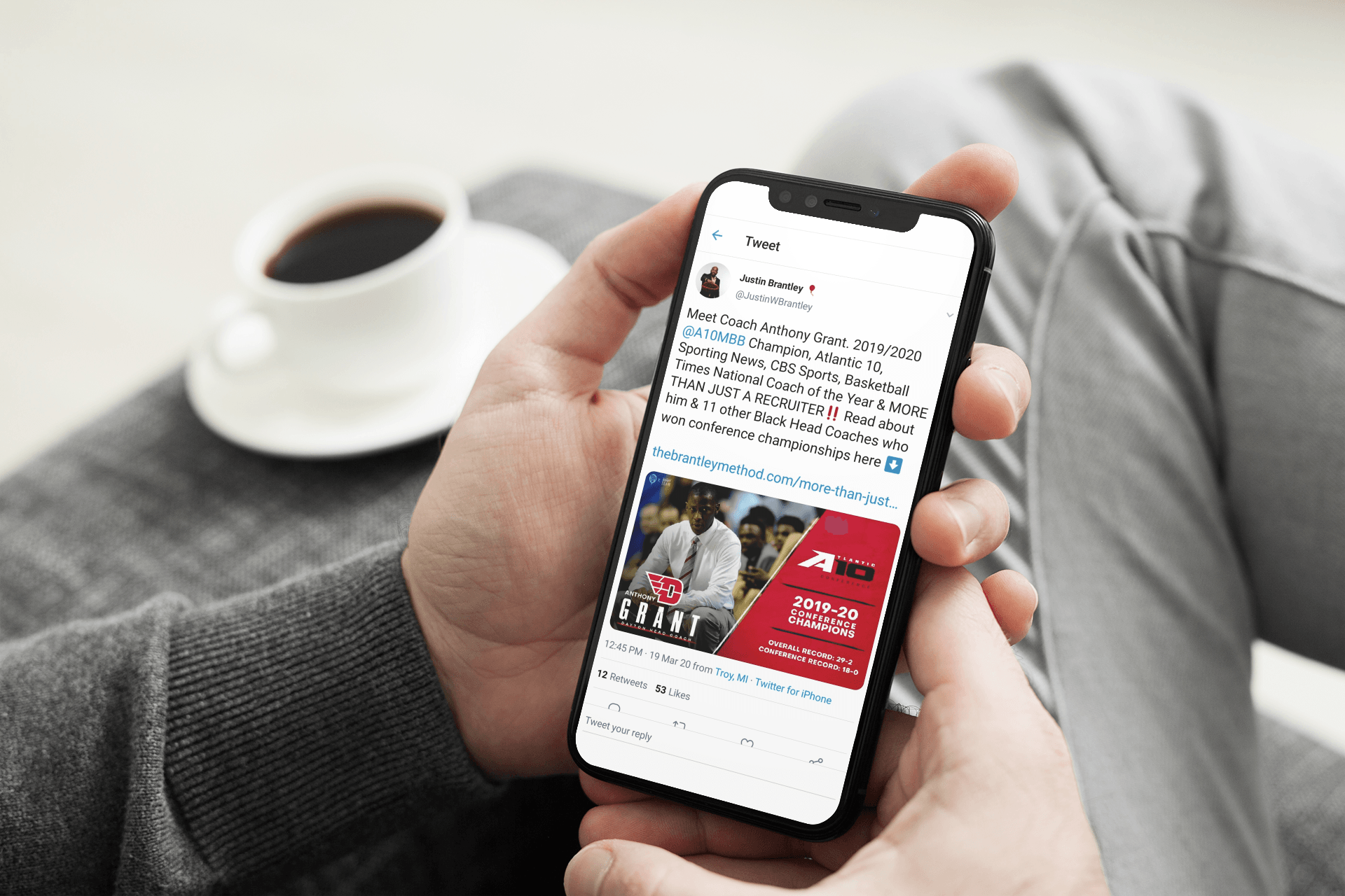 A person is holding a cell phone in their hand next to a cup of coffee.