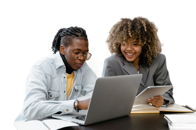Two people looking at laptop and tablet. One points at screen, other smiles.