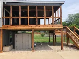 Elevated house deck with wooden posts, stairs, and a covered lower parking area
