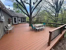 Spacious wooden deck with patio table, chairs, and railing beside a house and trees