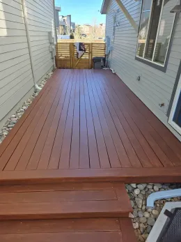 Wooden deck walkway between two houses leading to a gate, with a city view beyond.