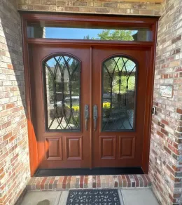 Front entry with reddish-brown double wooden doors, arched glass panes, and brick surround