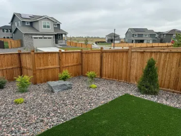 Backyard with wooden fence, gravel beds, and a green lawn in a suburban neighborhood.