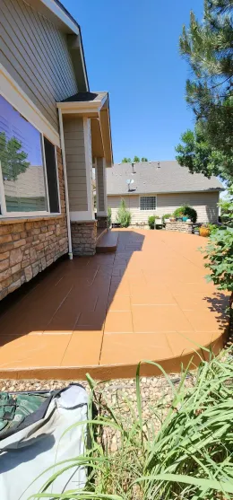 Brick house side yard with a curved orange patio, windows, and tall grass in the foreground