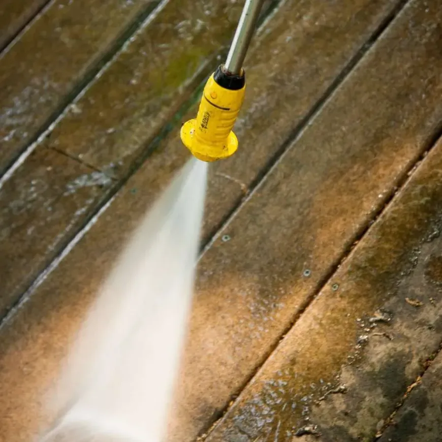 A yellow high pressure washer is spraying water on a wooden deck.