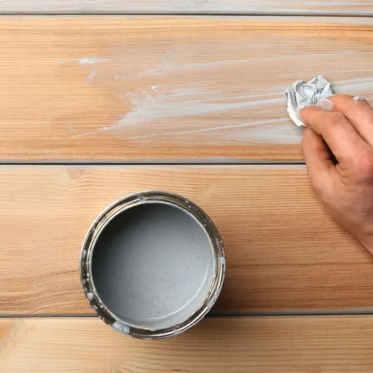 A person is cleaning a can of paint on a wooden table.