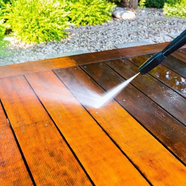 Pressure washer cleaning a wet wooden deck near a gravel garden border