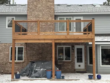 Snowy backyard patio with a wooden deck, brick chimney, sliding door, and covered items below