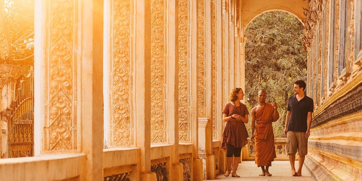 People walk with a monk along a decorated temple hallway.