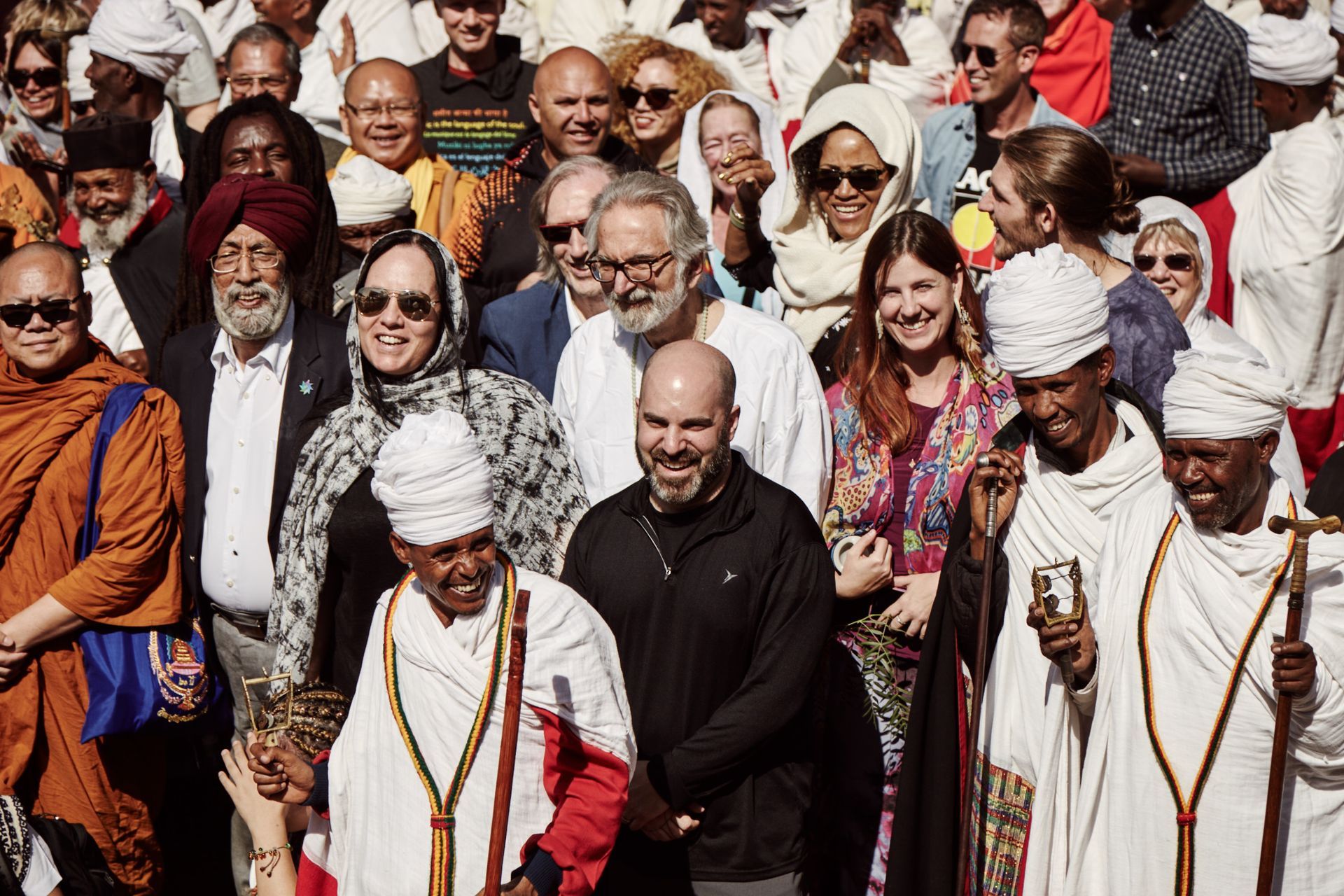 Group of diverse people smiling outdoors, some in religious attire.