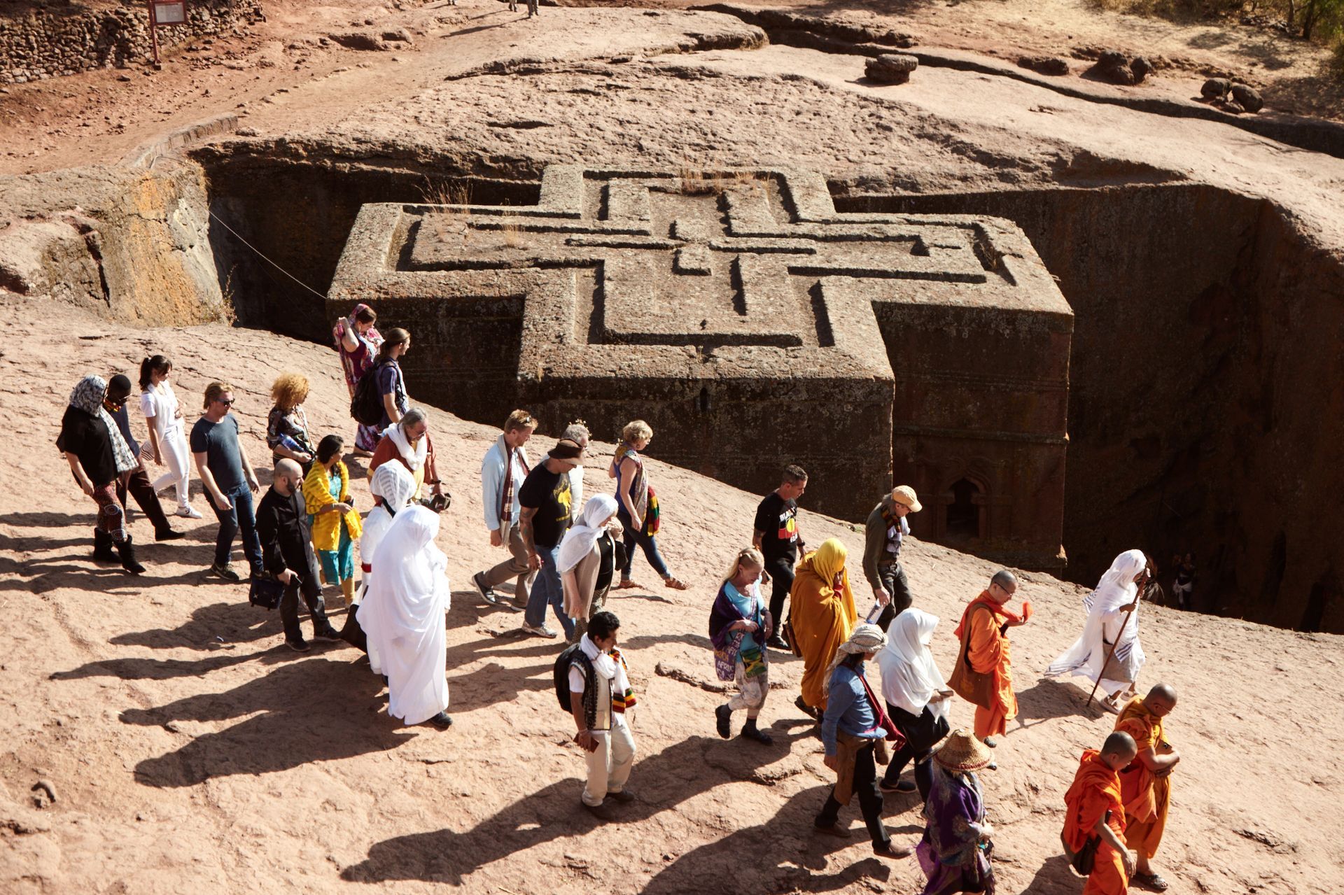 People stand near a large stone cross carved into a reddish-brown rock structure.