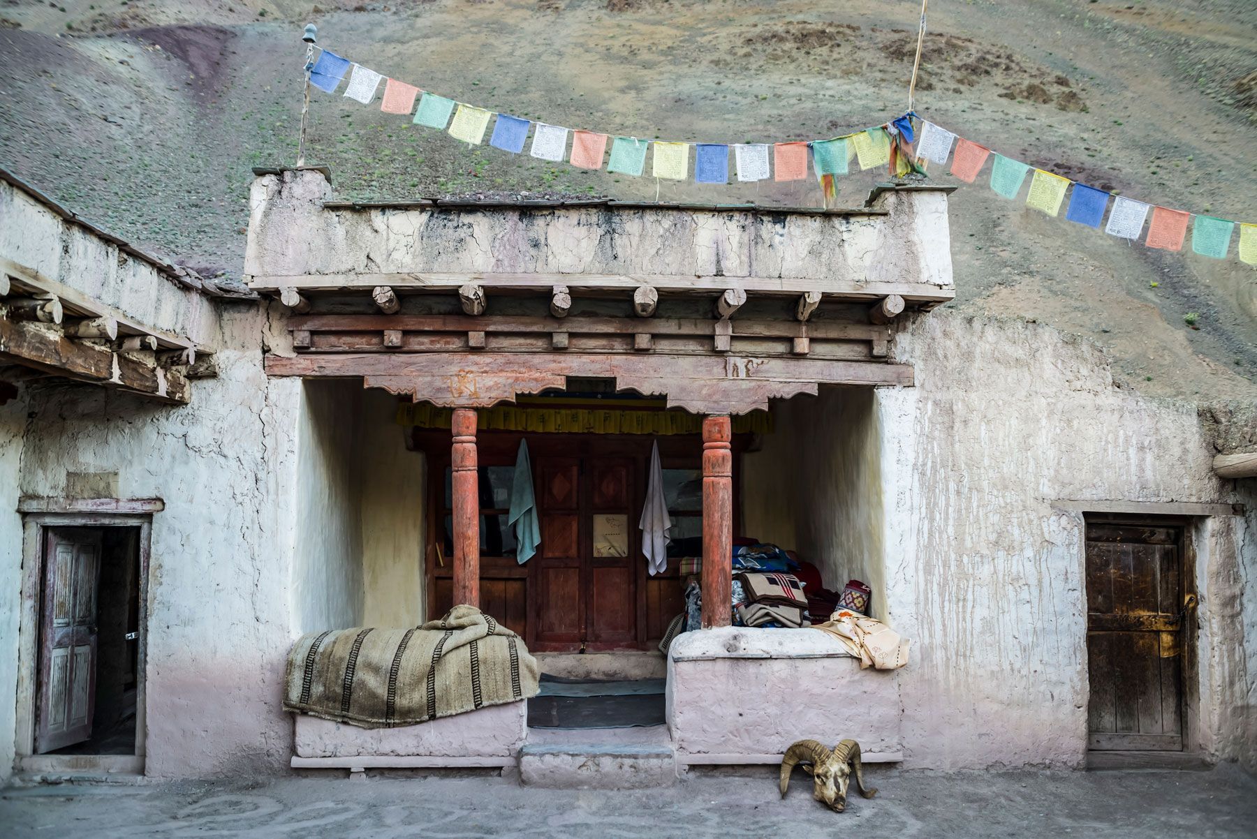 Exterior of a weathered building with a porch, prayer flags, and a dog in front.