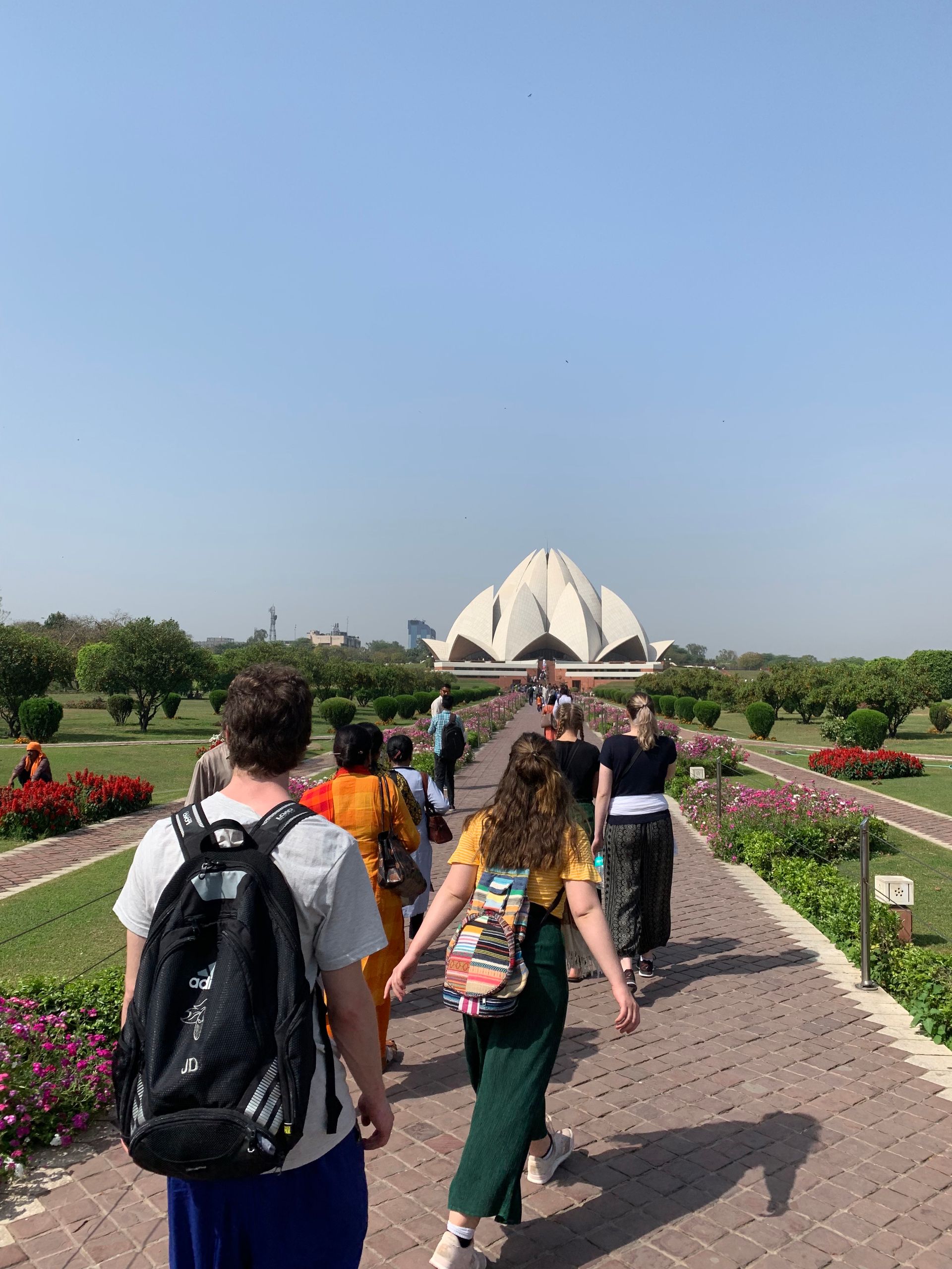 People walking toward a white, lotus-shaped temple on a sunny day.