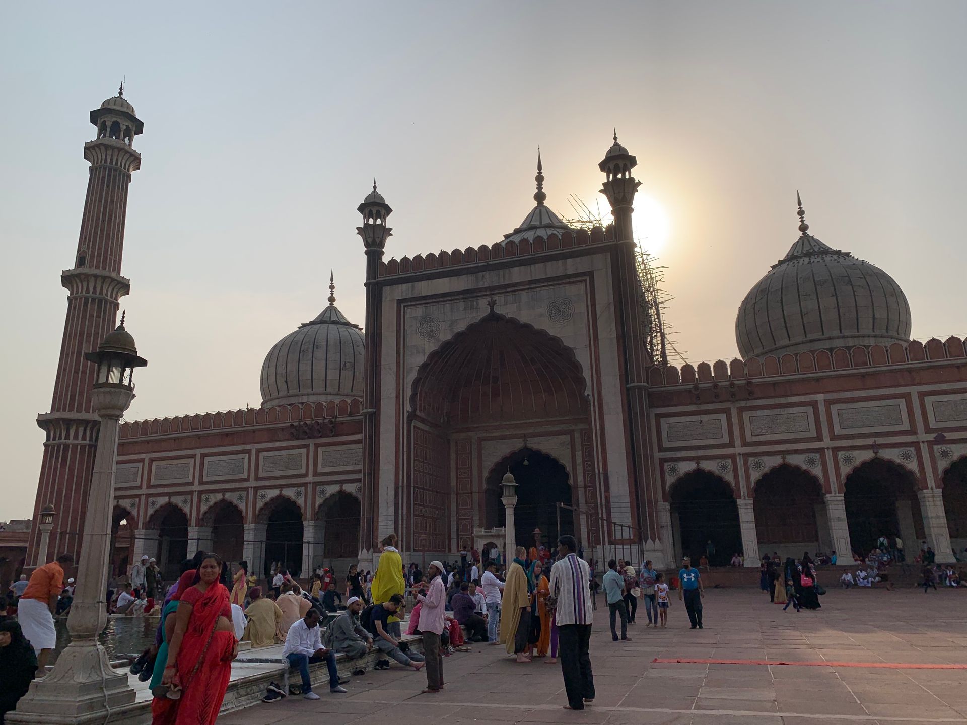 Jama Masjid, Delhi. People gather outside a large, red-brick mosque with domes and minarets in daylight.
