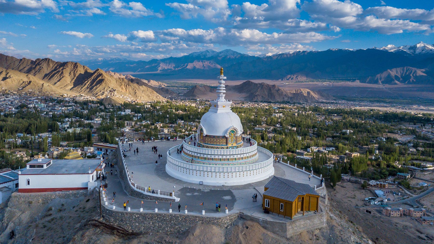 White Shanti Stupa atop a hill in Leh, India, overlooking a town and mountains.