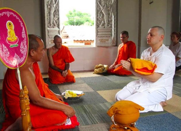 Men in orange robes and white attire in a temple, receiving an offering.
