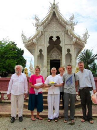 Group of people pose in front of a white ornate temple with a decorative roof, holding offerings.
