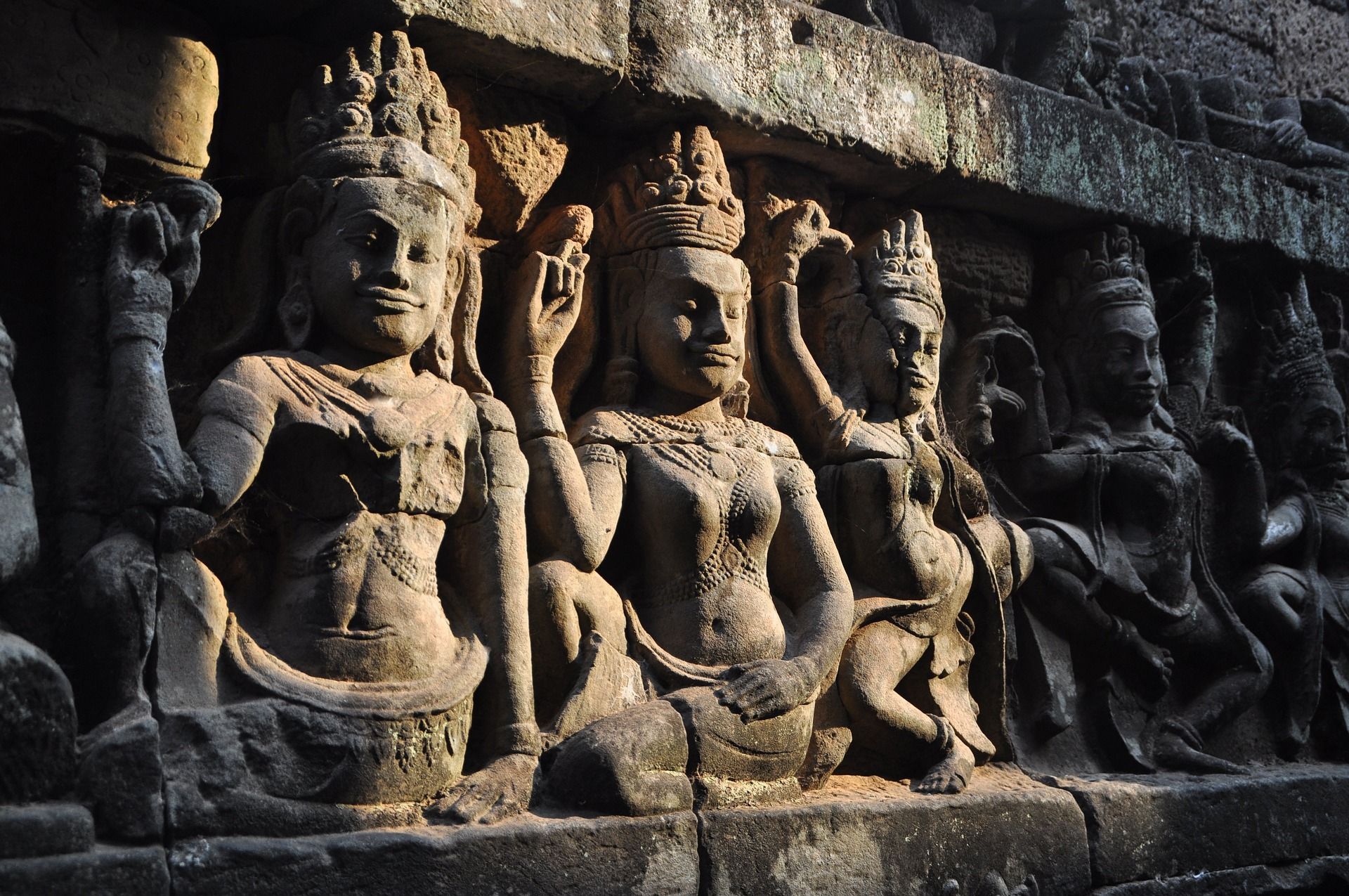 Stone carvings of apsaras at Angkor Wat, Cambodia. The figures are detailed and lit by sunlight.